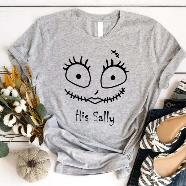Gray t-shirt with a face design and text 'His Sally' on a white surface with decorative items.