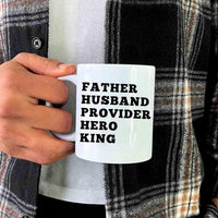 Person holding a mug with text 'FATHER HUSBAND PROVIDER HERO KING' against a plaid shirt background.