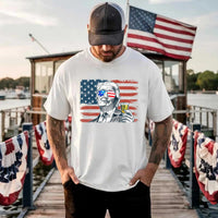 Man wearing a white t-shirt with a graphic design of a person holding a drink, with an American flag in the background, standing on a dock with American flags.