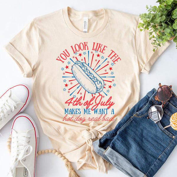 Beige t-shirt with 4th of July graphic design, paired with white sneakers and denim shorts on a light background.