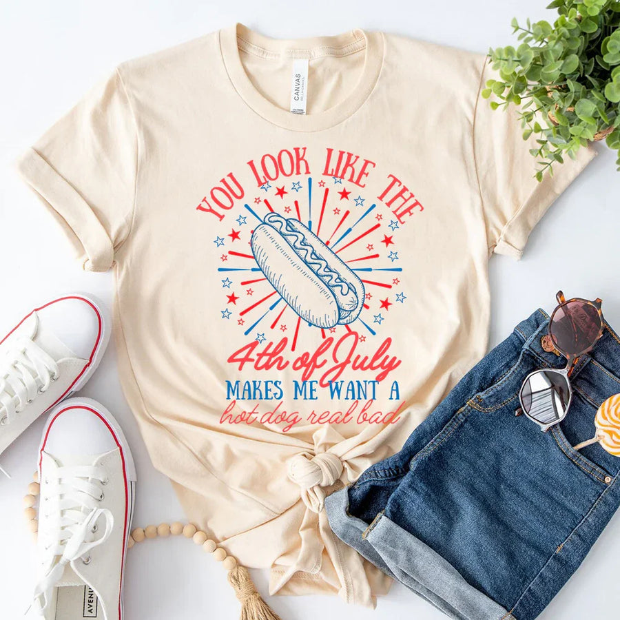 Beige t-shirt with 4th of July graphic design, paired with white sneakers and denim shorts on a light background.
