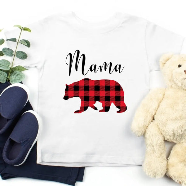 May include matching family t-shirts featuring a Christmas bear design, laid flat with festive decorations and greenery.