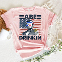 Pink t-shirt with Abraham Lincoln holding a drink, USA flag sunglasses, and 'Abe Drinkin' text