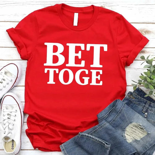 Red t-shirt with 'BET TOGE' text, paired with jeans and sneakers on a wooden surface.