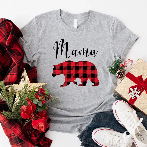 May include matching family t-shirts featuring a Christmas bear design, laid flat with festive decorations and greenery.