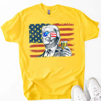 Yellow t-shirt with a graphic of a person holding a drink and wearing sunglasses with American flag design, paired with white sneakers.