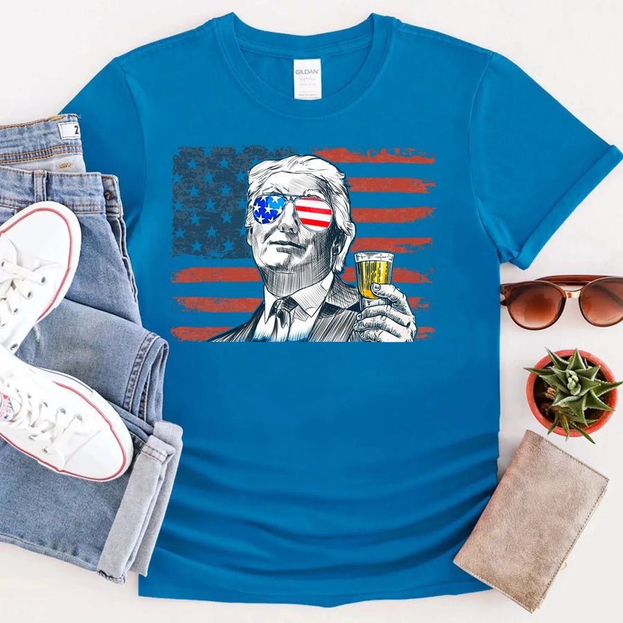 Blue t-shirt with a graphic design of a person holding a drink, surrounded by jeans, sneakers, sunglasses, and a plant.