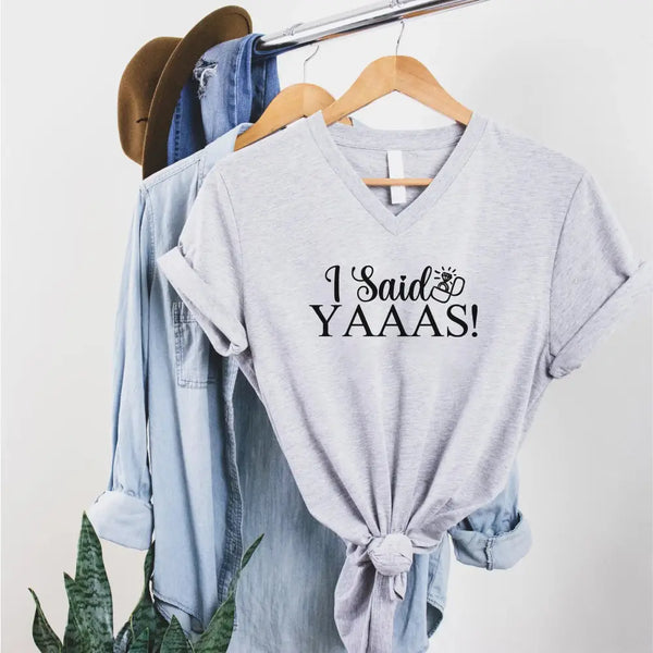 Light gray t-shirt with 'I Said YAAAS!' text on a hanger with denim jacket and hat.