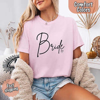 Light pink oversized t-shirt with black “Bride” script and a small heart, styled with denim shorts and a cozy cream jacket, labeled “Comfort Colors” and “Fast Shipping.”