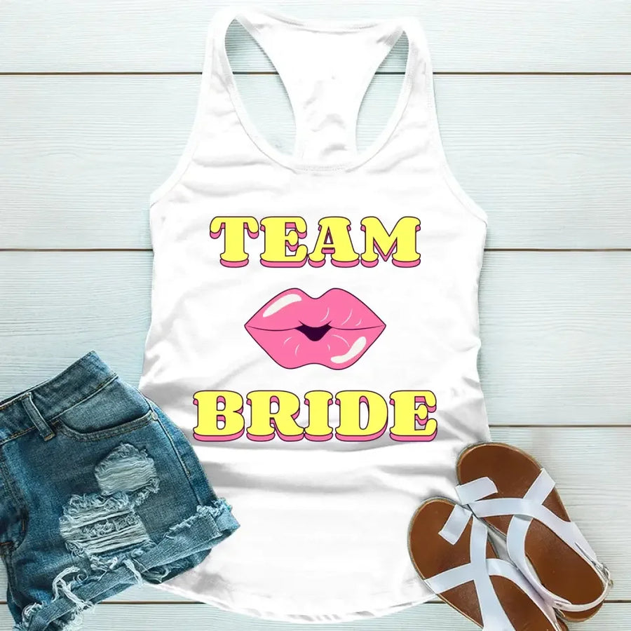 A white tank top with 'TEAM BRIDE' text and a heart symbol replacing the word 'TEAM'. The tank top is displayed alongside denim shorts and white sandals, suggesting a casual outfit for a bachelorette party.