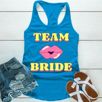 A blue tank top with 'TEAM BRIDE' text and a heart symbol replacing the word 'TEAM'. The tank top is displayed alongside denim shorts and white sandals, suggesting a casual outfit for a bachelorette party.