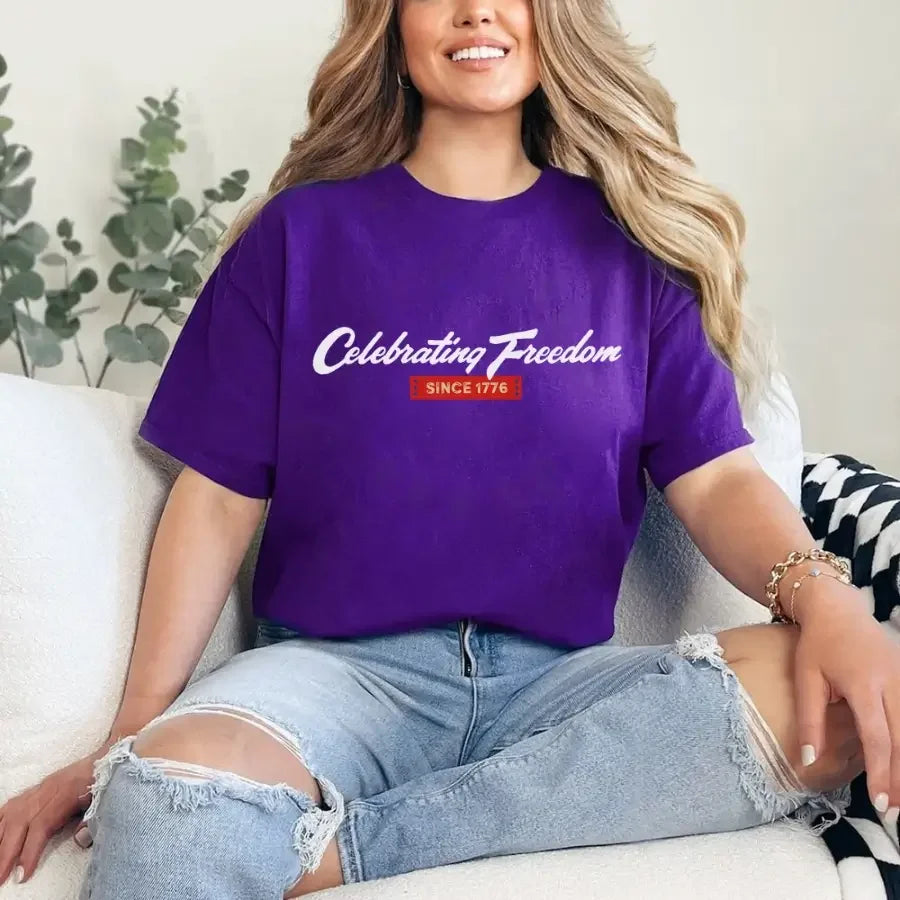 Person wearing a purple t-shirt with 'Celebrating Freedom Since 1776' text, sitting on a couch.
