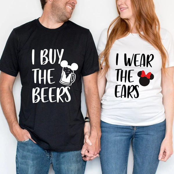 A man and a woman wearing matching black T-shirts with text. The man's shirt reads 'I BUY THE BEERS' and the woman's shirt reads 'I WEAR THE EARS'.