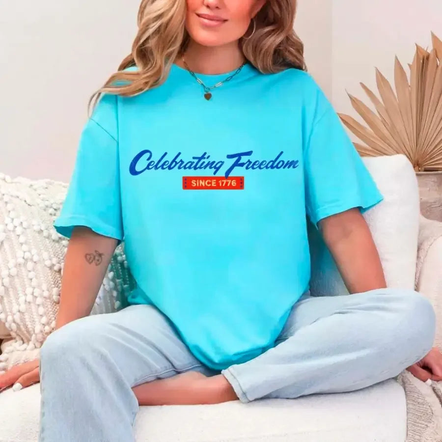 Person wearing a blue t-shirt with 'Celebrating Freedom Since 1776' text, sitting on a white couch.