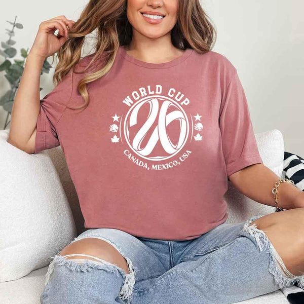 May include a person wearing a Mauve colored 2026 World Cup T-shirt featuring bold soccer graphic and relaxed fit.