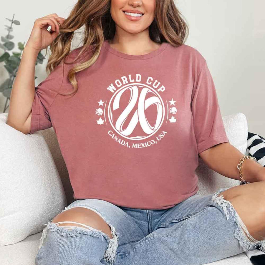 May include a person wearing a Mauve colored 2026 World Cup T-shirt featuring bold soccer graphic and relaxed fit.