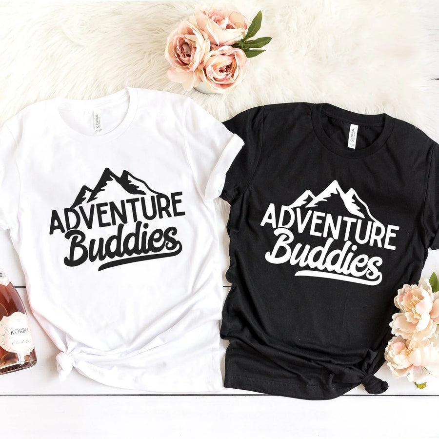 Black and white Adventure Buddies t-shirts with mountain design, flat lay with flowers